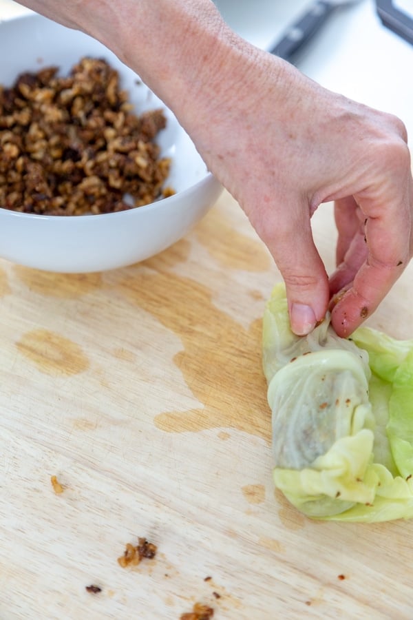 A hand rolling a cabbage leaf over beef filling.