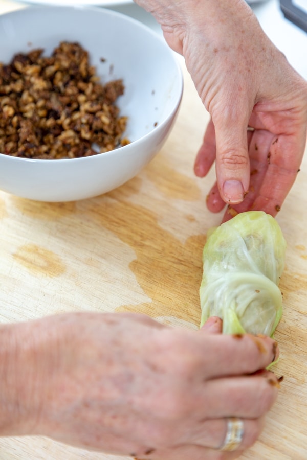 Two hands rolling a filled cabbage leaf and tucking the ends into the sides of the leaf.