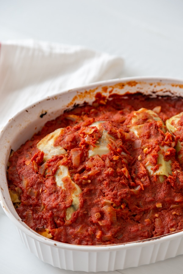 A white baking dish with cabbage rolls and tomato sauce. 