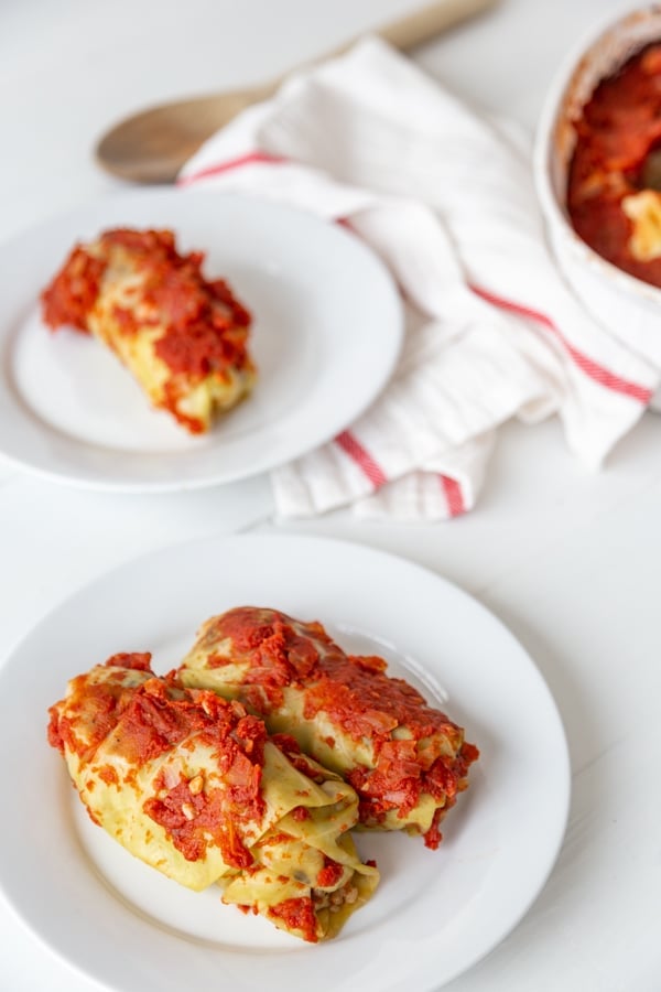 2 white plates with stuffed cabbage rolls and tomato sauce and a white and red striped towel. 