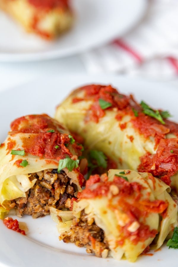 Stuffed cabbage rolls on a white plate and one is cut in half. 