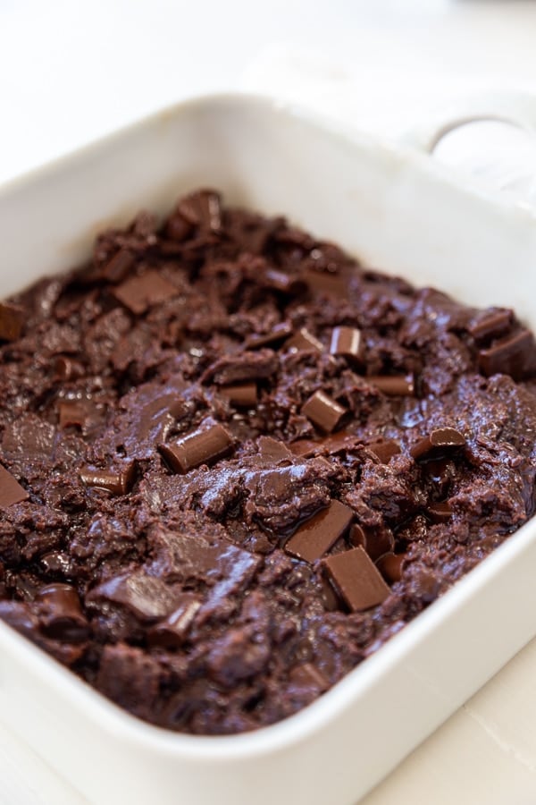 Brownie batter with chocolate chunks in a square white baking dish.