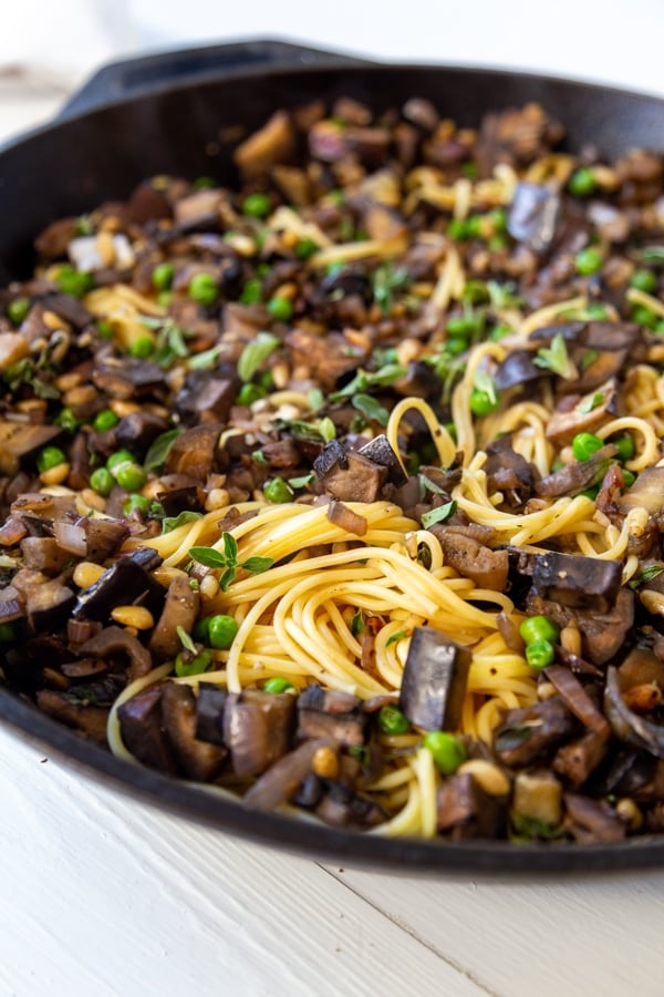 An iron skillet filled with spaghetti and eggplant and peas.