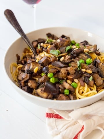 A white bowl with spaghetti and eggplant with a fork in the bowl.