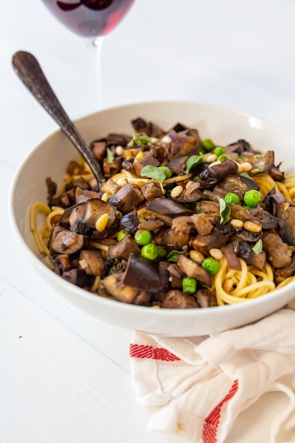 A white bowl with spaghetti and eggplant with a fork in the bowl. 