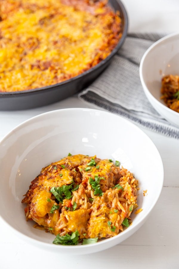 2 white bowls filled with Mexican casserole and the casserole in the background.