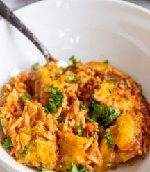 A white bowl with a pasta casserole and silver fork.