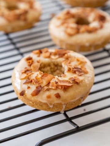 Doughnuts with coconut bacon chips on top cooling on a wire rack.