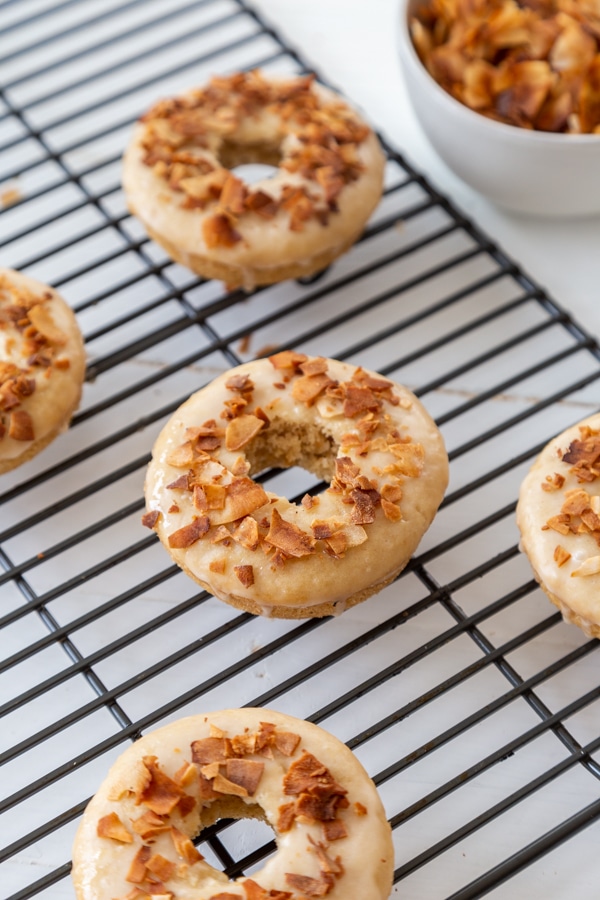 Coconut bacon and maple glazed doughnuts on a cooling rack with a bowl of coconut bacon next to the rack. 