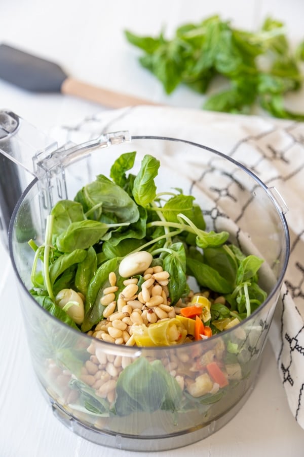 A food processor with ingredients for pesto.