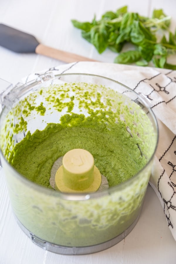 A food processor with green pesto sauce.