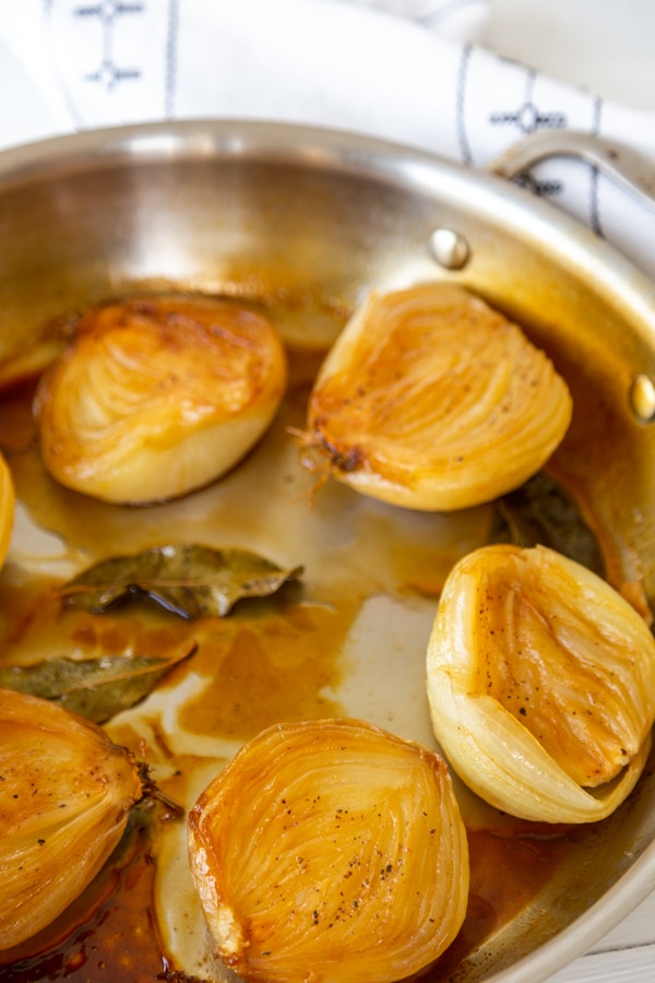 A round pan with caramelized baked onions in broth with bay leaves.