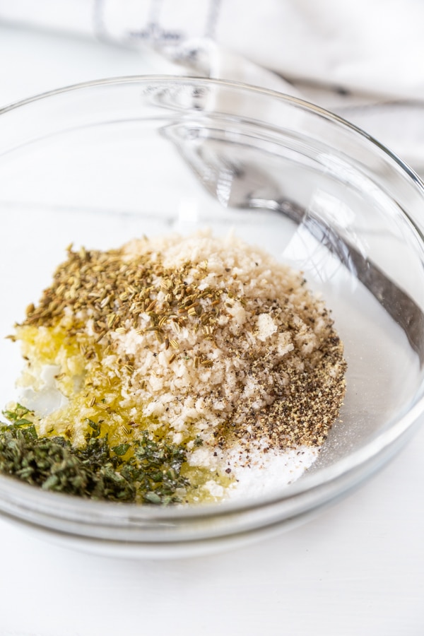 A clear glass bowl with breadcrumbs and spices.