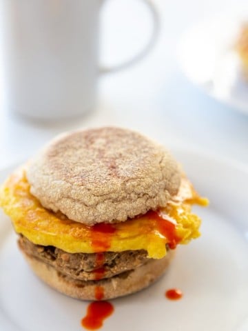 A sausage, egg, and cheese breakfast sandwich with hot sauce dripping down the sandwich.