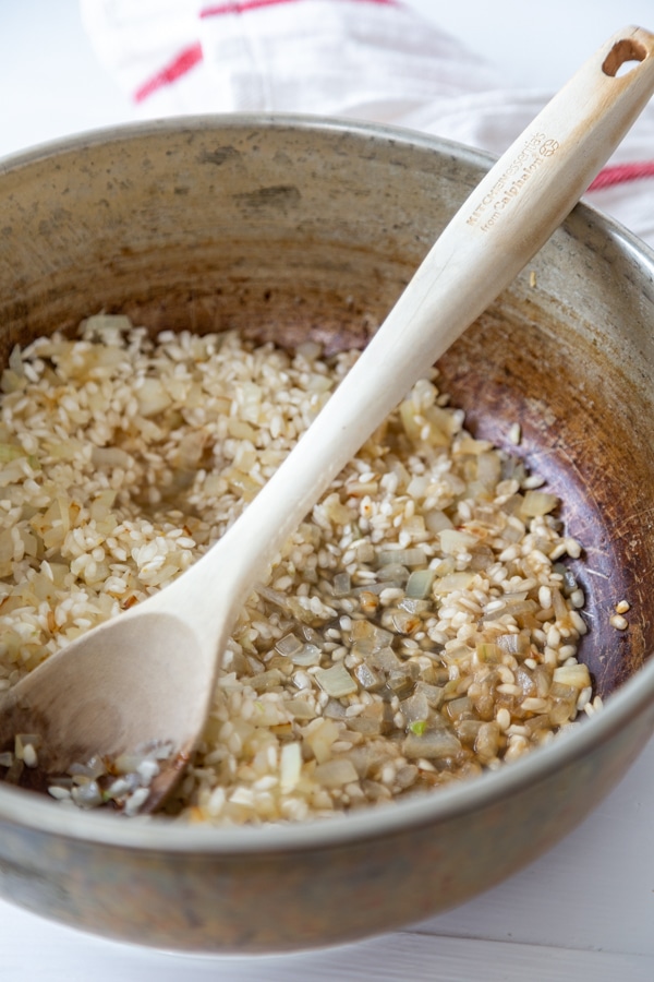 A copper pan with arborio rice and a wooden spoon. 