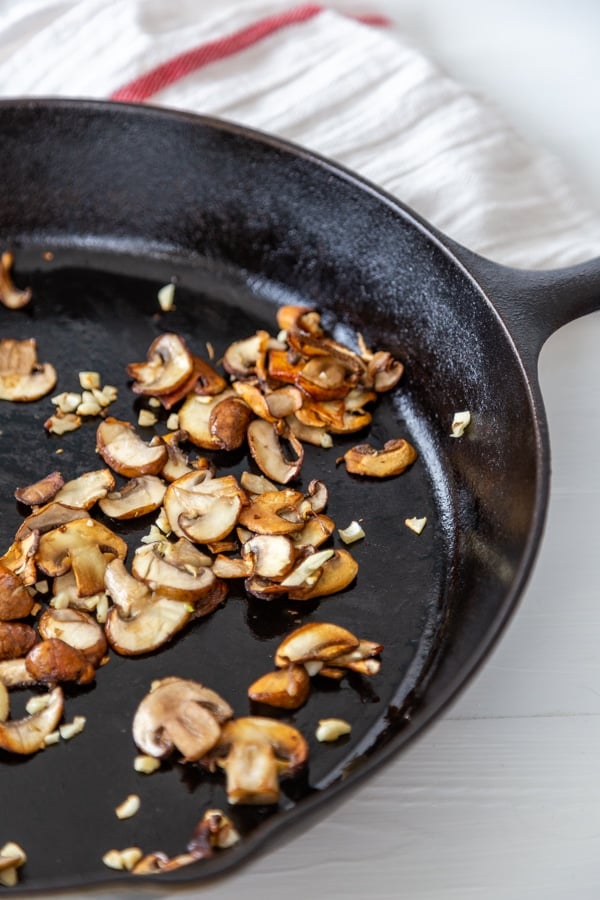 An iron skillet with cooked sliced mushrooms and garlic.