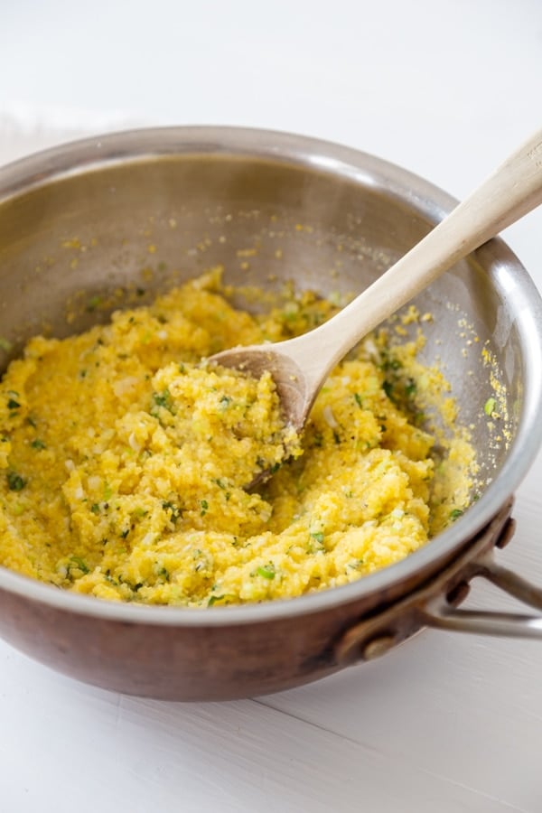 A copper pot with polenta mixed with herbs and a wooden spoon. 