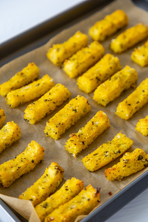 A baking sheet with herbed polenta fries on parchment paper. 