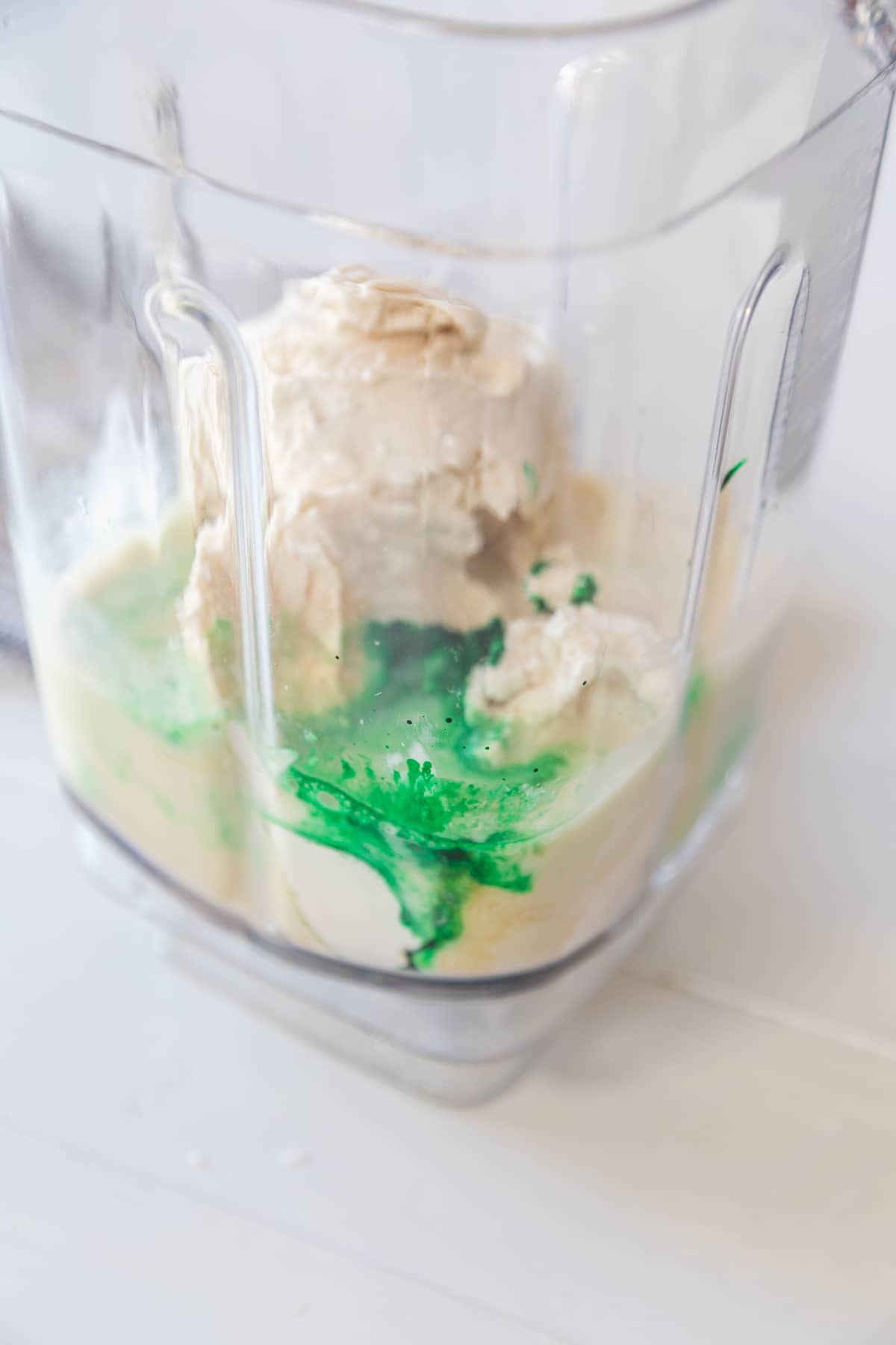 A blender pitcher with vanilla ice cream, milk, and green food dye. 