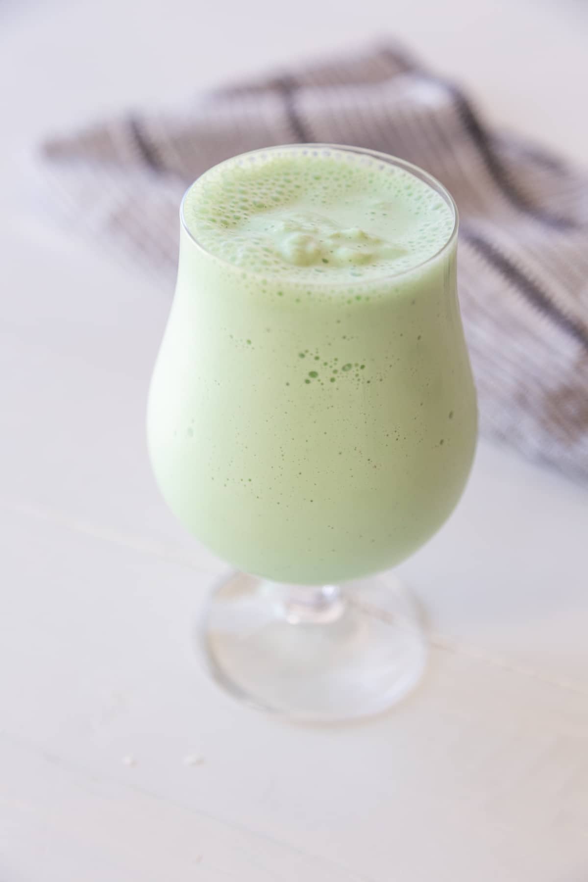 A green milkshake in a glass with a white and black towel behind the glass. 