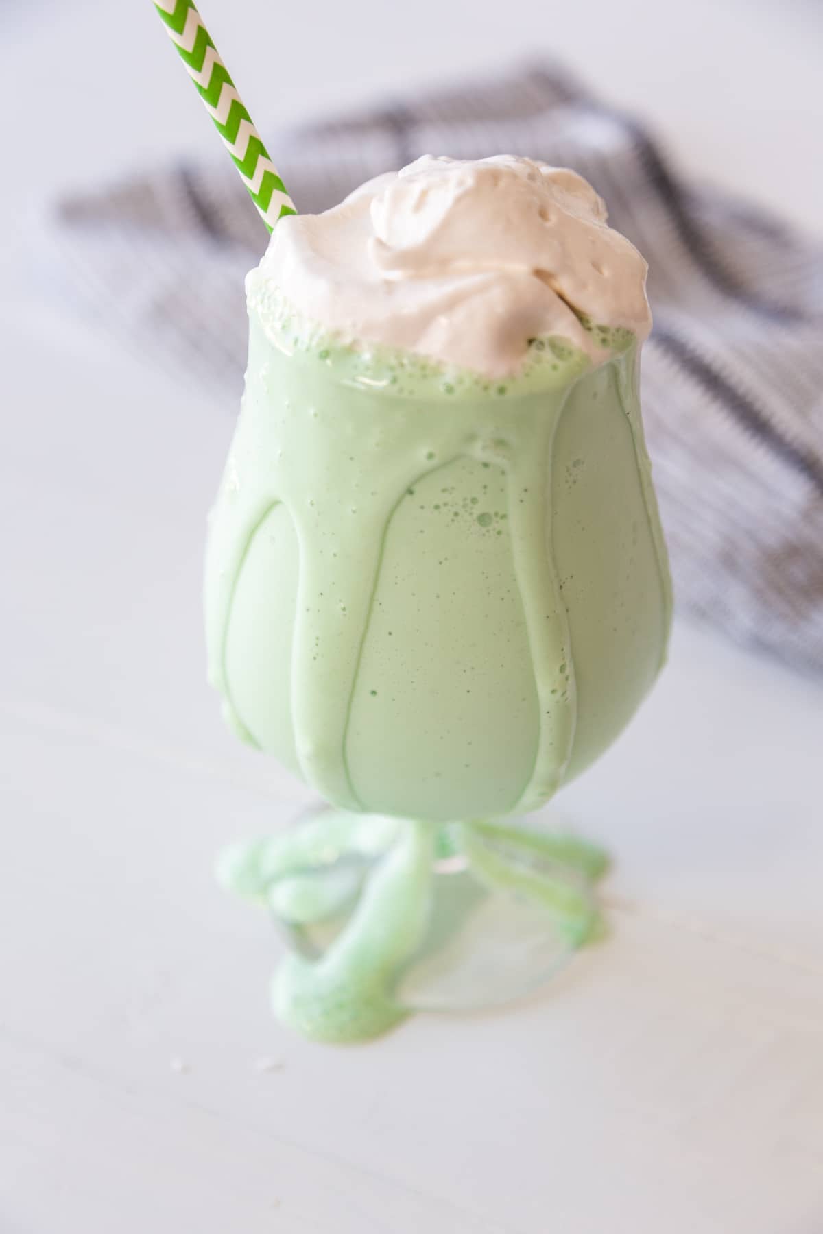 A green milkshake with whipped topping dripping down a glass.