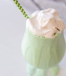 A green shamrock shake with whipped topping in a glass with a green and white straw.