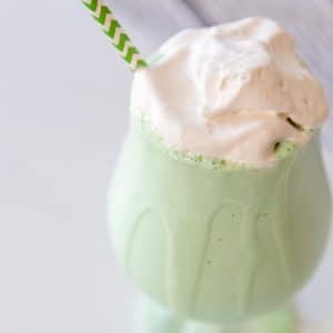 A green shamrock shake with whipped topping in a glass with a green and white straw.
