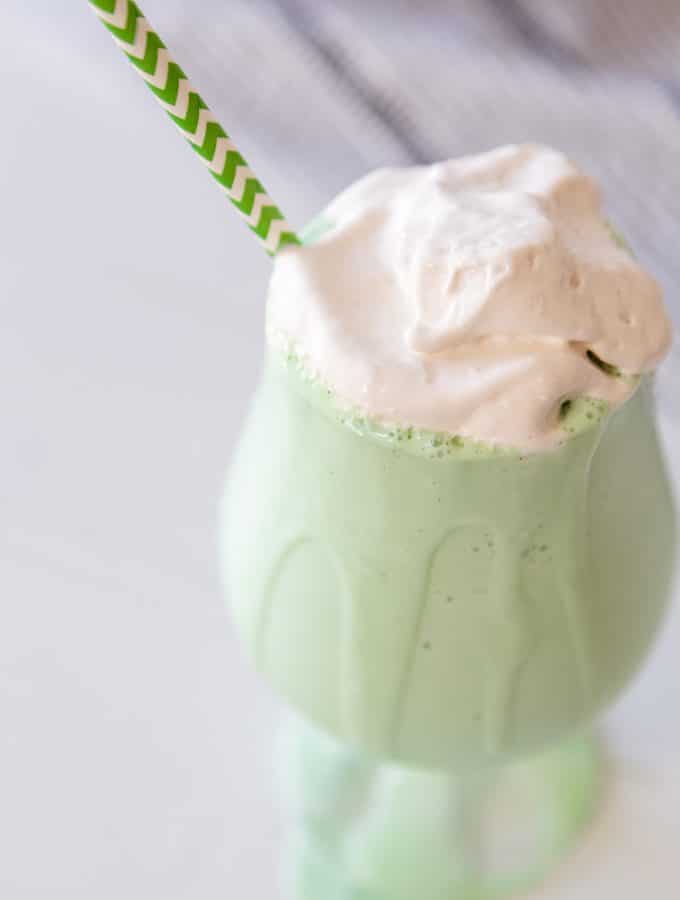A green shamrock shake with whipped topping in a glass with a green and white straw.
