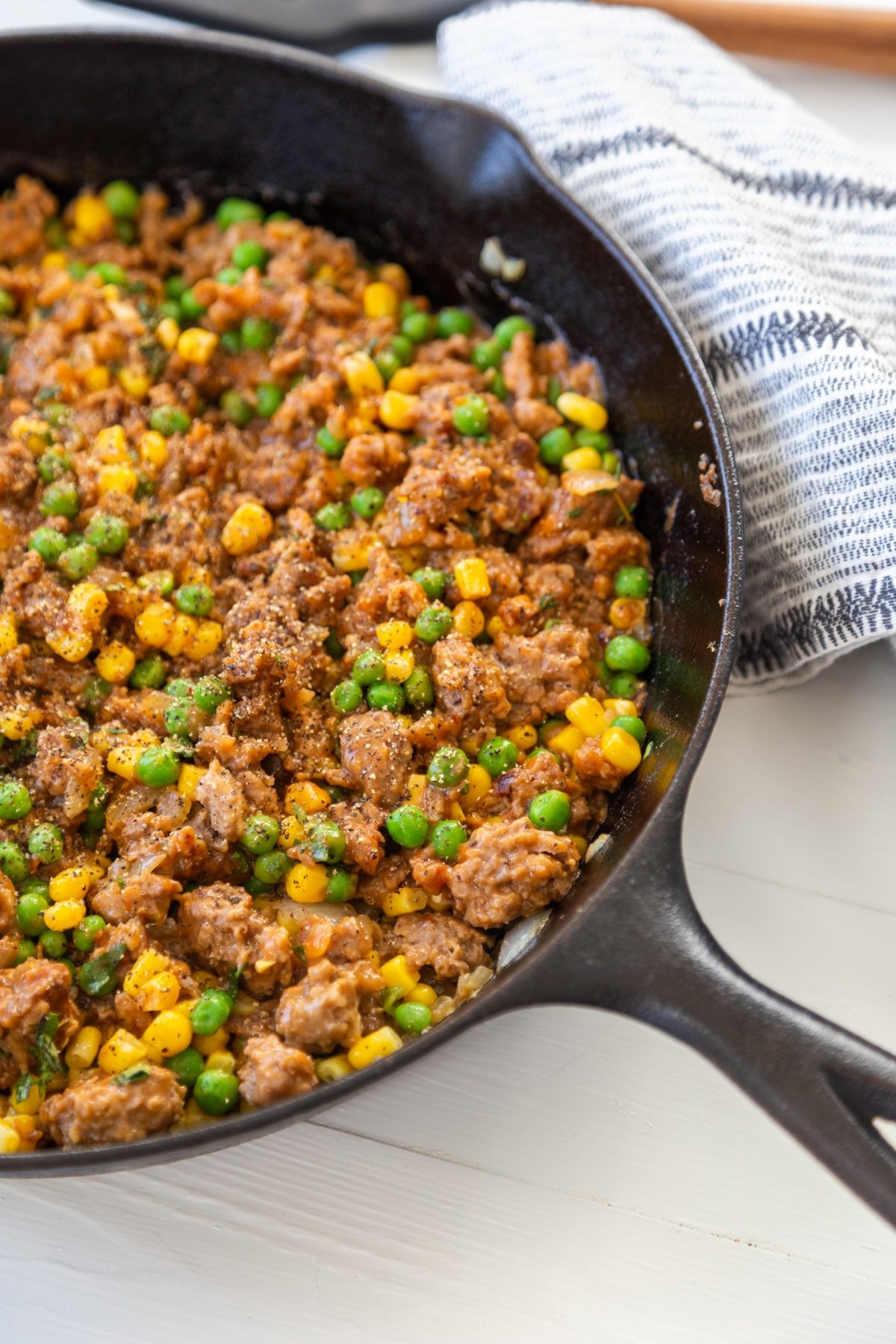 An iron skillet filled with ground meat, peas, and corn. 