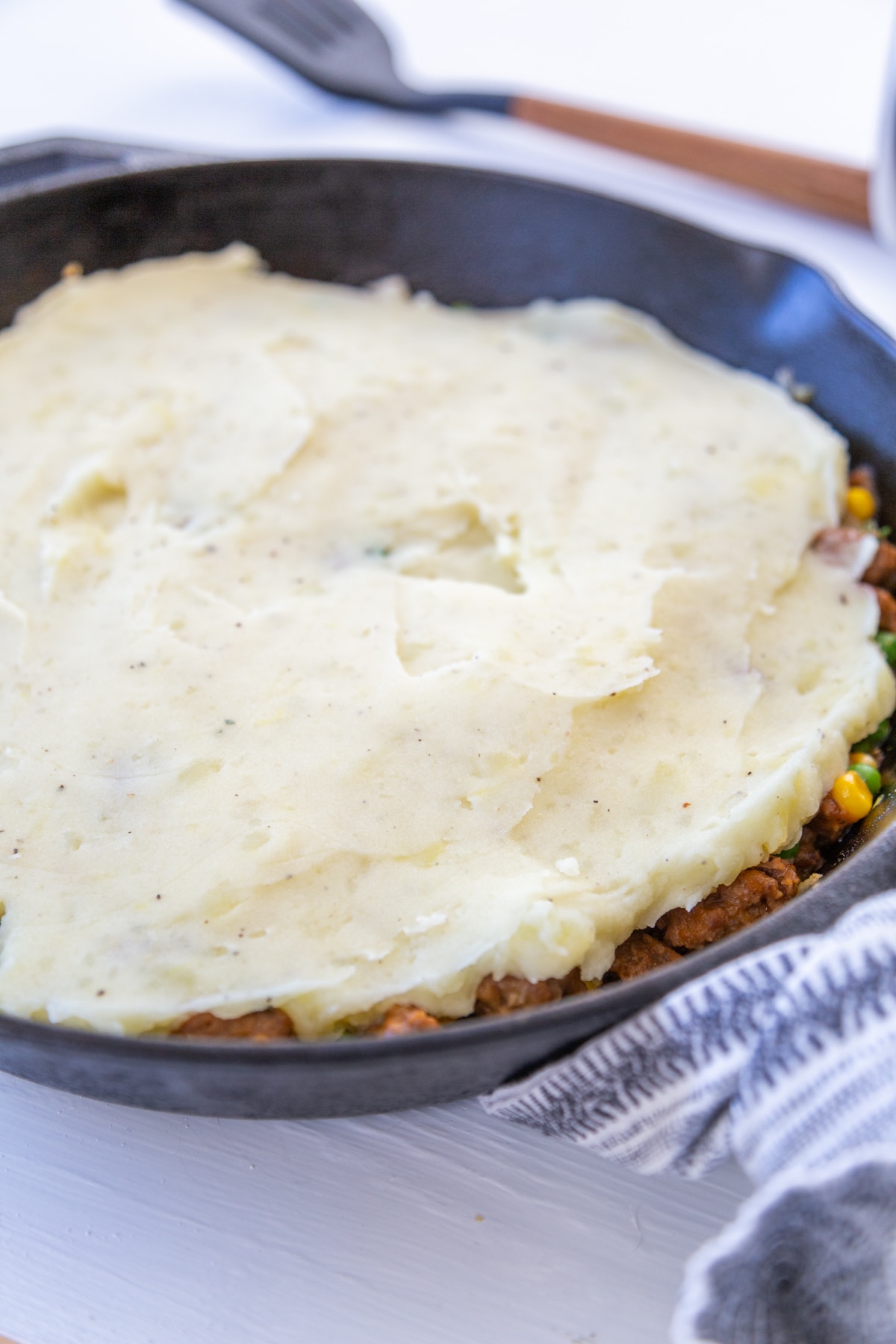 An iron skillet with meat and vegetables and whipped potatoes spread over the top.