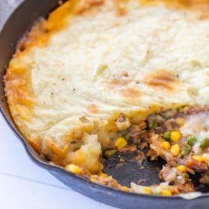 An iron skillet with a sheperd's pie and a portion removed from the pan.