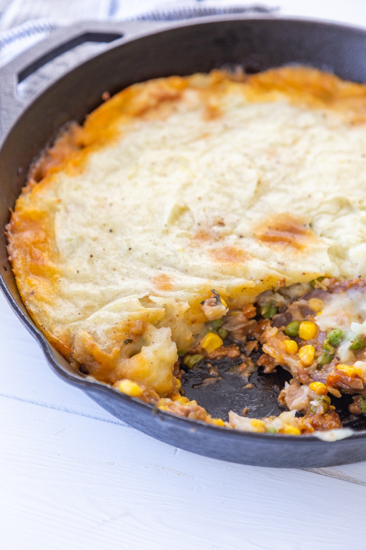 An iron skillet with a sheperd's pie and a portion removed from the pan.