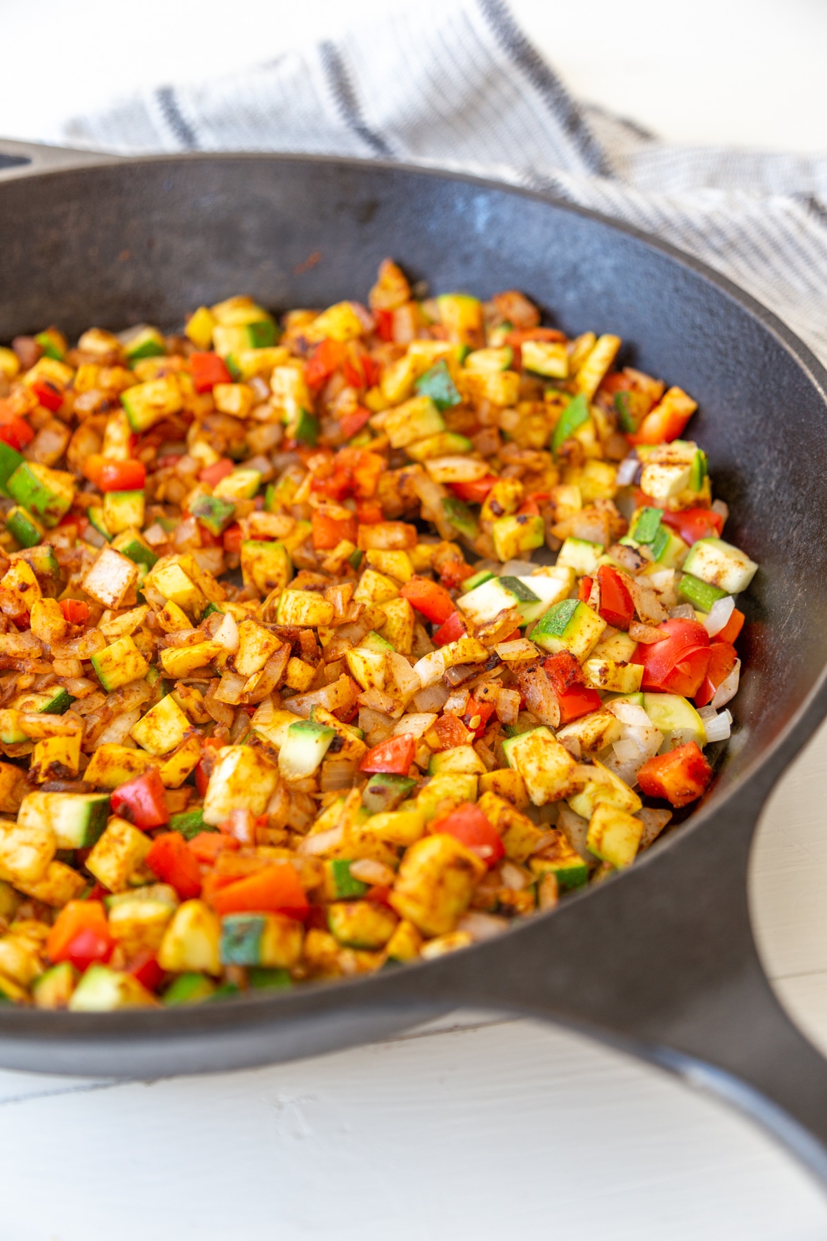 An iron skillet filled with spicy diced zucchini, yellow squash, and bell pepper. 