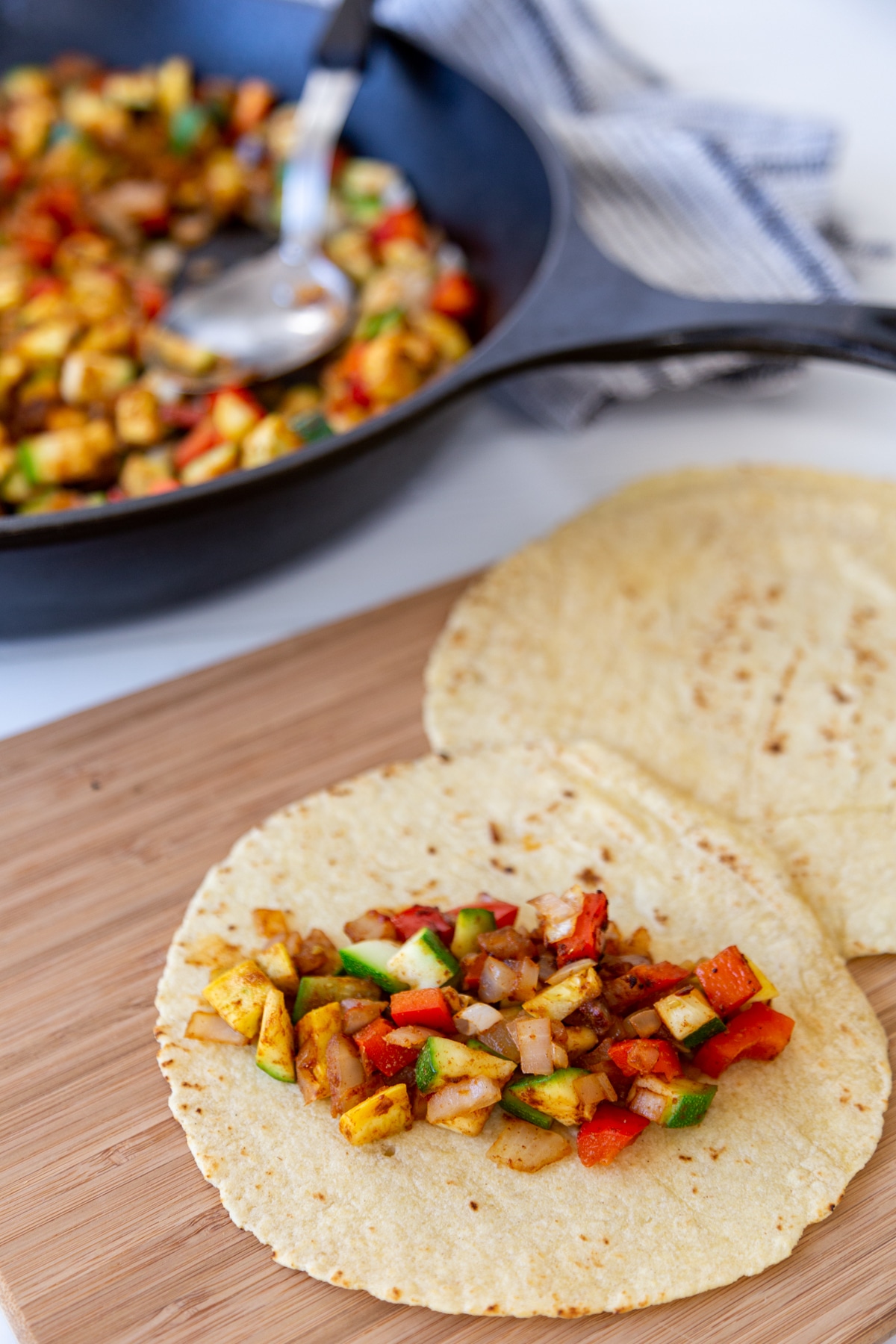 A tortilla with spicy zucchini, yellow squash, and bell pepper in the center and a skillet of the veggies in the background. 