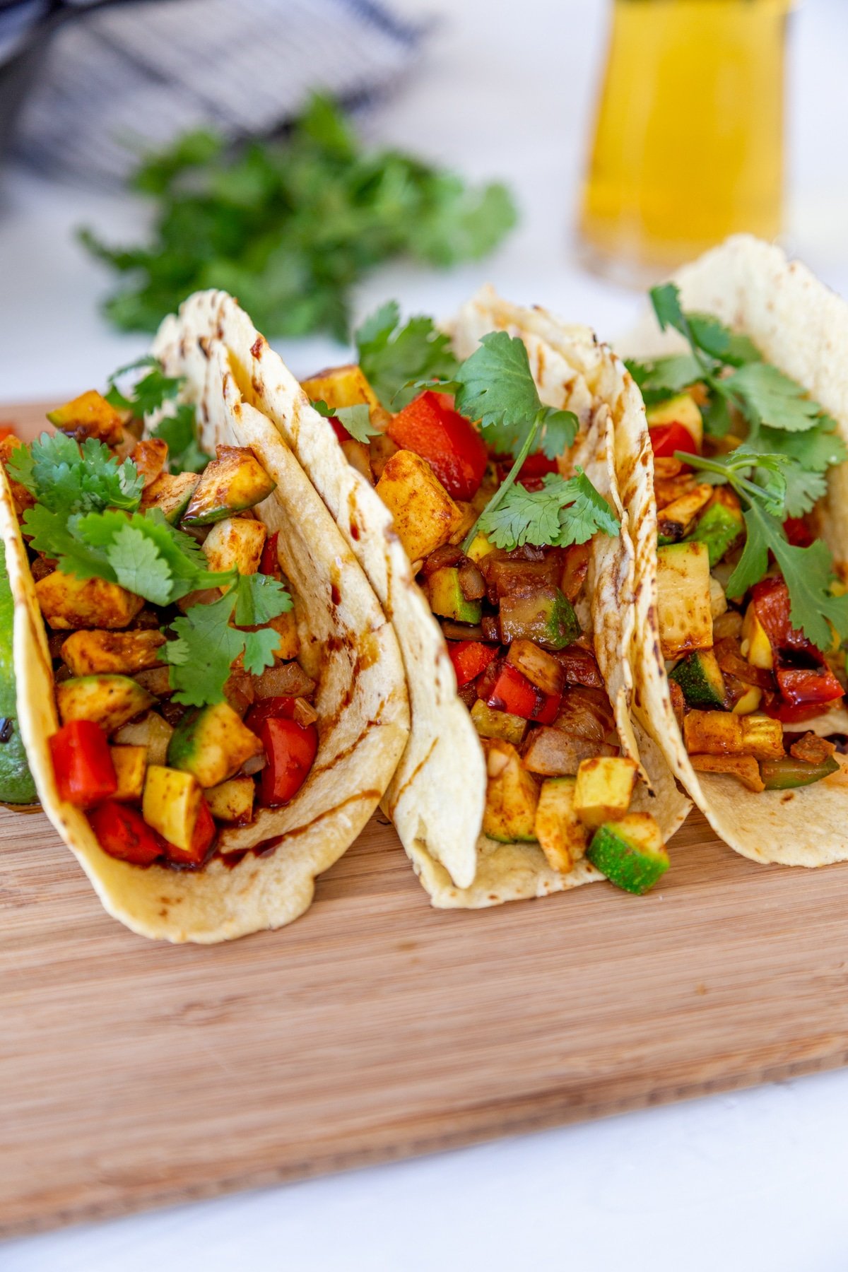 3 veggie tacos on a wood board with a glass of beer in the background. 