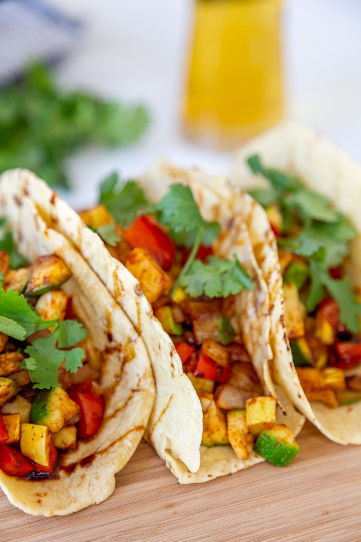 Three tacos with spicy veggies and cilantro with a beer behind them. 