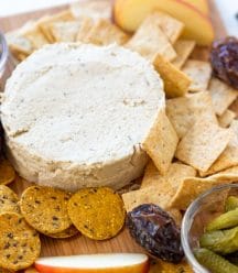 A cheese board with a round piece of spreadable cheese, crackers, and fruit.
