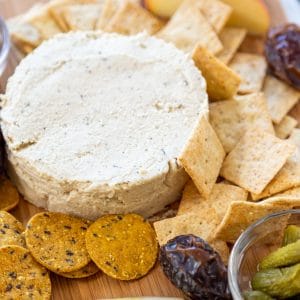 A cheese board with a round piece of spreadable cheese, crackers, and fruit.