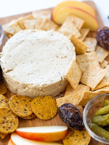 A cheese board with a round piece of spreadable cheese, crackers, and fruit.