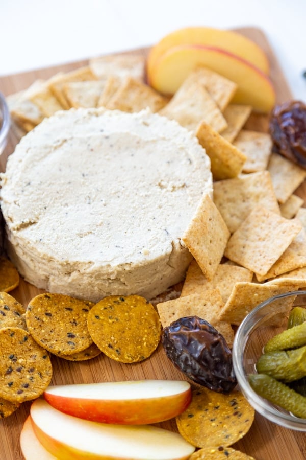 A cheese board with a round piece of spreadable cheese, crackers, and fruit.