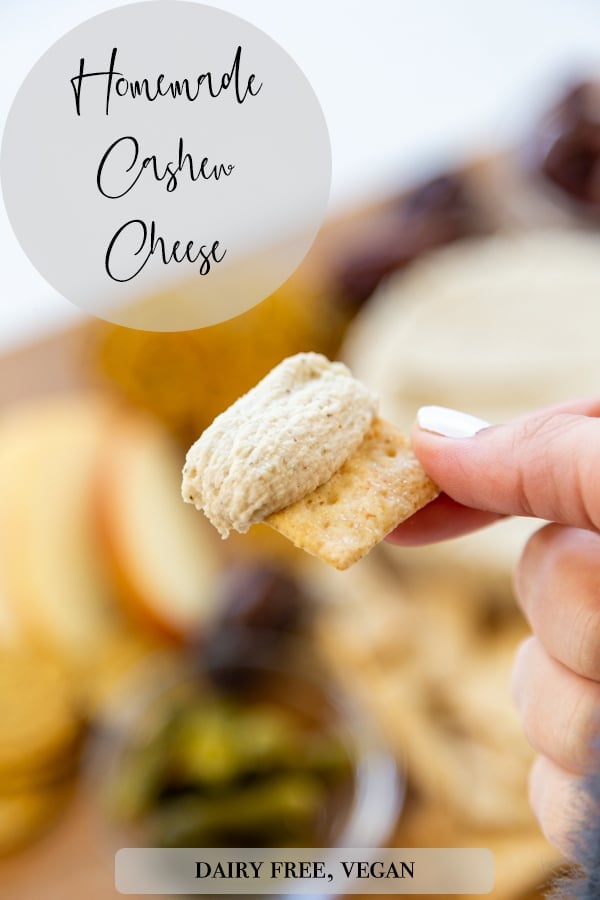 A Pinterest pin for vegan cashew cheese with a picture of a hand holding a cracker with the cheese. 