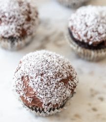 A marble board with 4 chocolate frosted cupcakes with shredded coconut on the tops.