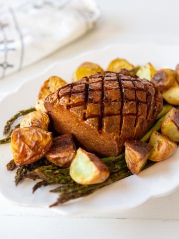 A sliced vegan ham on a bed of asparagus on a white platter with potatoes.