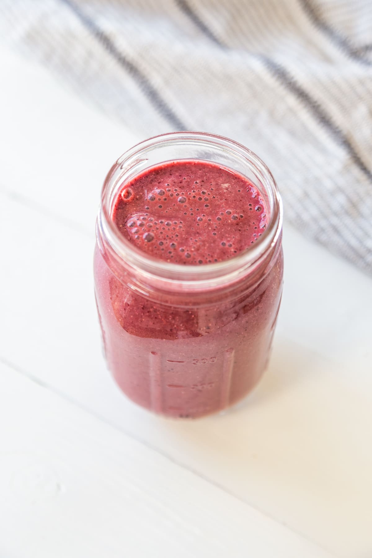 A cherry smoothie in a mason jar with a white and black towel next to the glass. 