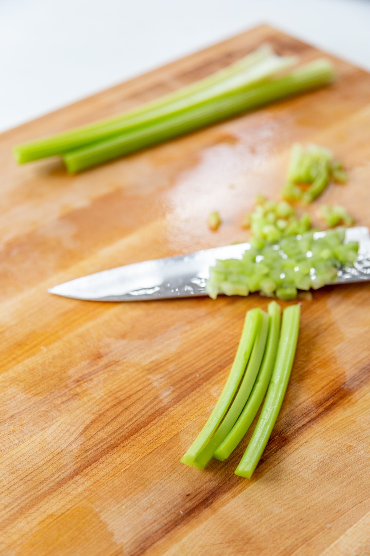 A wood cutting board with a knife, celery sticks, and chopped celery.