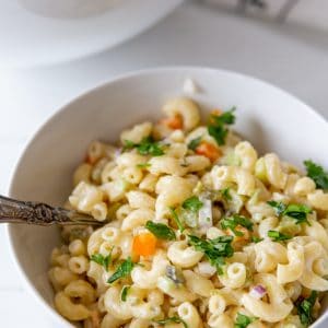 A white bowl with macaroni salad and a silver spoon sticking out of the salad.