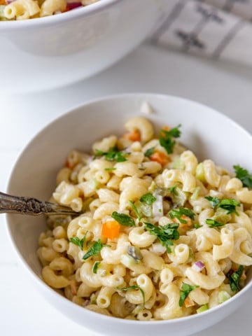 A white bowl with macaroni salad and a silver spoon sticking out of the salad.