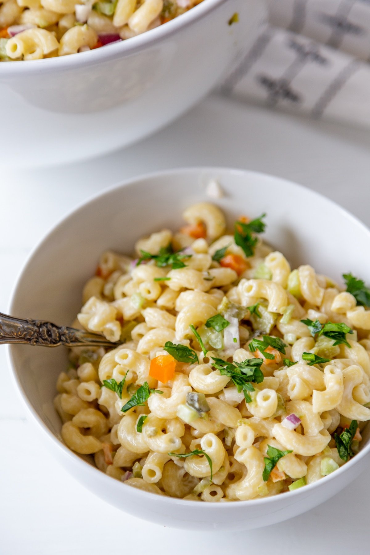 A white bowl with macaroni salad and a silver spoon sticking out of the salad. 