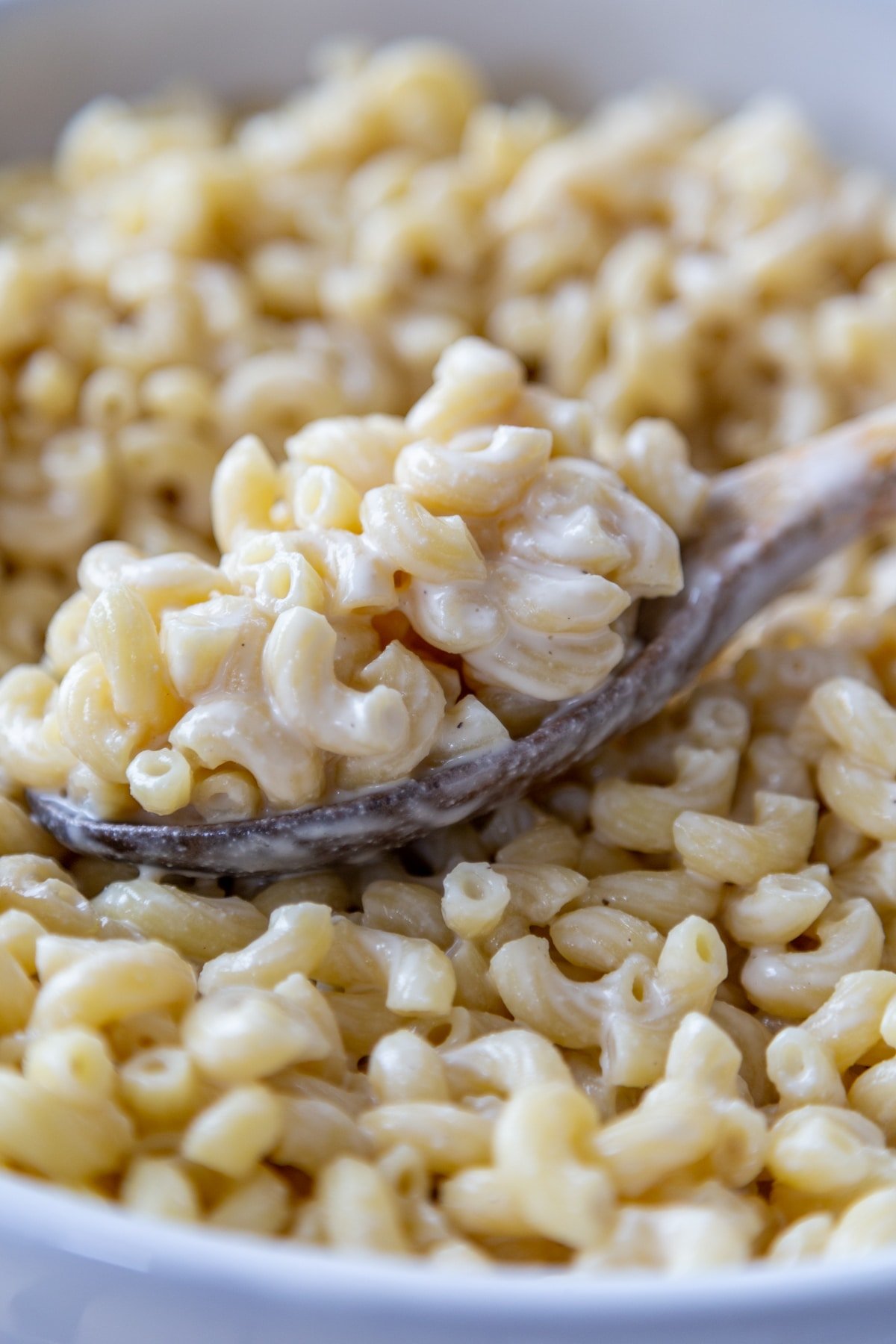 A bowl with macaroni and a creamy dressing and a spoon full of the noodles.