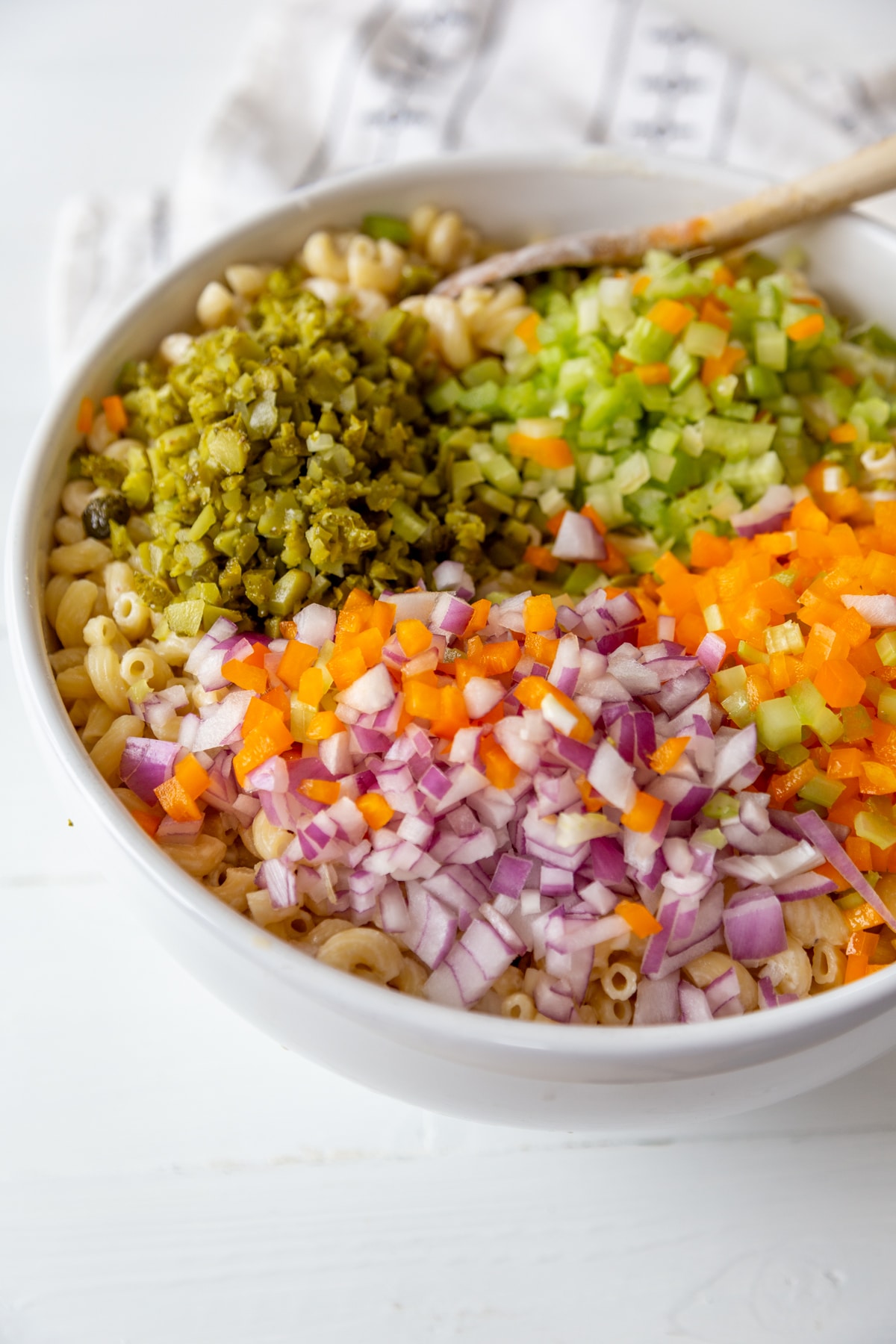 A large white bowl with macaroni, dressing, and chopped vegetables.
